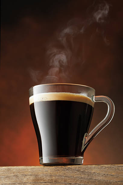 Steam rises from transparent cup of hot coffee standing on table against brown background