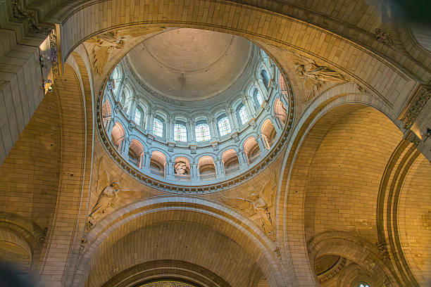 Paris, France - October 14, 2025,The interior of the Sacre-Corur Basilica in Montmartre reveals a solemn and spiritual atmosphere, with decorated vaults, classical columns, and gilded frescoes framing the central dome. The softly filtered natural light enhances the architectural symmetry and the sacred character of the space. Ideal for tourism, editorial, and cultural content about religious heritage, sacred art, and monumental architecture.