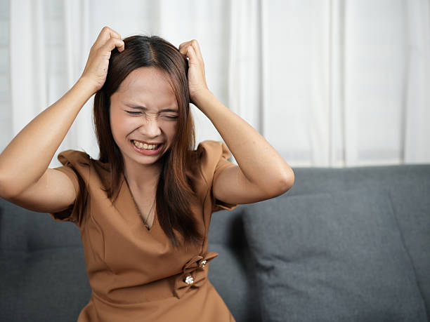 istock Woman expressing frustration while sitting on couch, with her hands in her hair. setting is indoors, featuring soft lighting and neutral color palette 2244424831