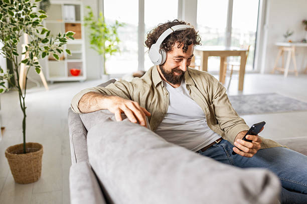 istock Cheerful Guy Enjoying Music and Browsing Smartphone Indoors 2244427147