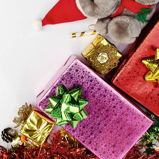 A vibrant collection of wrapped Christmas presents, festive ribbons, and a Santa hat are artfully arranged on a clean white surface.