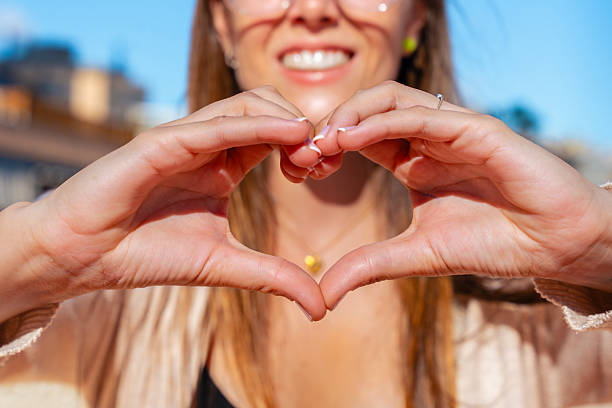 istock Woman making heart shape with hands outdoors, smiling in sunlight. 2244428842