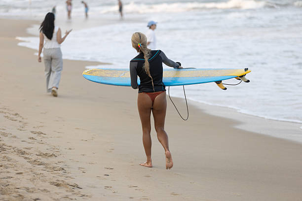 23 March 2025, Da Nang - Vietnam.Young woman is walking on the beach after surfing in Da Nang, enjoying the city’s long coastline. Beaches like My Khe and My An are popular favorites for both relaxation and recreational activities.