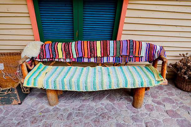 A rustic wooden bench with wagon wheels as supports, set on a lush green lawn with a backdrop of trees and foliage, creating a picturesque countryside setting
