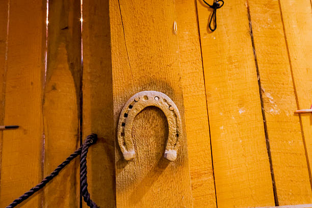 A set of old metal horseshoes displayed on a warm yellow wooden barn interior, including single and clustered pieces nailed or hanging on beams, with aged patina and cobwebs that emphasize rural craftsmanship and folk good‑luck symbolism.