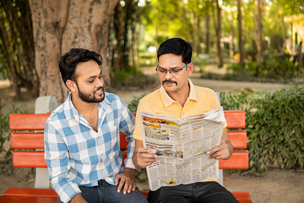 istock Mature Indian father and young son reading a newspaper together while sitting on park bench in fresh air. 2244432854