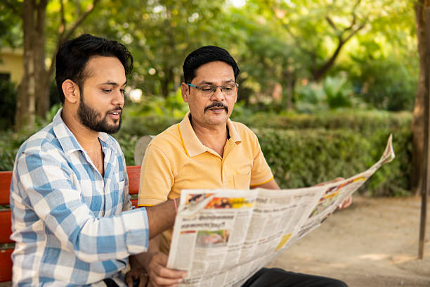 istock Mature Indian father and young son reading a newspaper together while sitting on park bench in fresh air. 2244432856