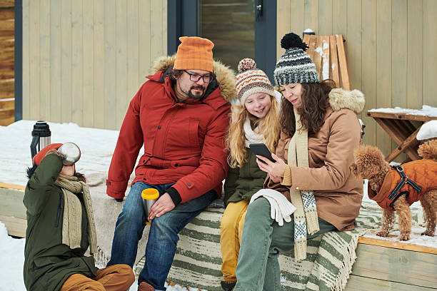 istock Family Sitting Outdoors Smiling and Using Smartphone during Winter 2244434933