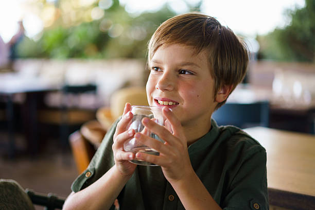 Smiling boy holding a glass and looking away while sitting at a restaurant.