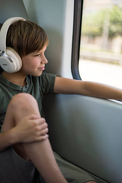 istock Boy listening to music while traveling by train looking out window. 2244435162