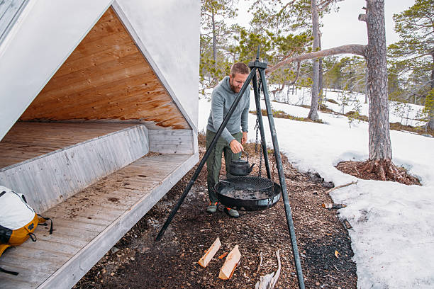 Man Preparing Campfire Kettle Near Shelter in Snow