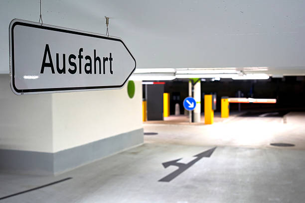 istock Sign on parking garage ceiling says: Exit (German: Ausfahrt). Barrier also gate and blue sign in the depth of field. 2244442850