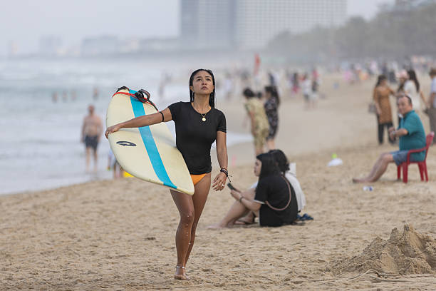 04 April 2025, Da Nang - Vietnam.Young woman is walking on the beach after surfing in Da Nang, enjoying the city’s long coastline. Beaches like My Khe and My An are popular favorites for both relaxation and recreational activities.