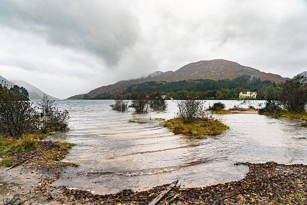 Scottish highlands landscape showing mountains, a loch, and an old building on a cloudy day