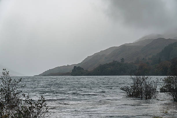 Glencoe mountains covered in mist with rough lake water under an overcast sky