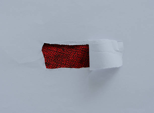istock Hole in white torn paper revealing red background. 2244444776