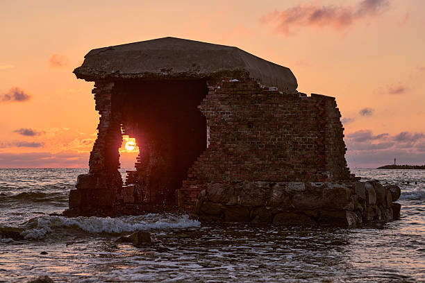 Ancient stone ruins bathed in sunset glow stand resilient against ocean waves, evoking nostalgia and serenity in coastal setting, abandoned Western Fort in Baltiysk