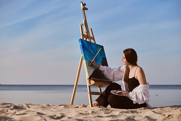 istock Young female painter creating beach art in peaceful setting 2244445321