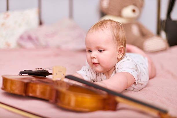 istock Curious baby girl examines violin on soft pink bedspread 2244445331
