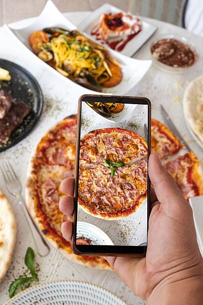 istock Hand holding smartphone photographing pizza on restaurant table 2244451431