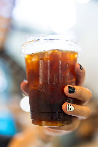 Hand holding to go plastic cup with iced black coffee