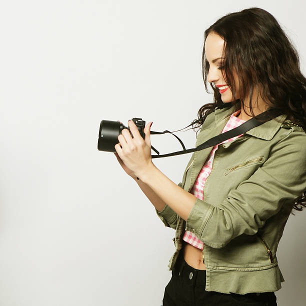 Beautiful young woman with camera over gray background