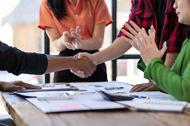 istock Business partners shaking hands at a meeting while their coworkers are clapping, celebrating the closing of a deal or a successful agreement. 2244464400