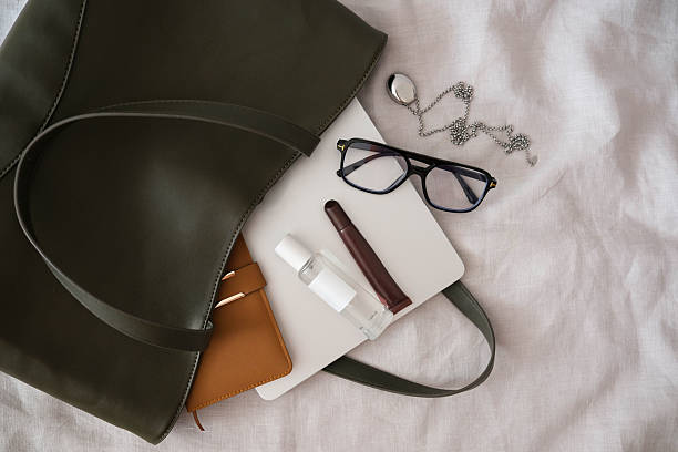 istock A stylish and chic green bag that is filled with all the essential items you need for work and daily activities of woman - notebook, glasses, copybook, handcream, perfume,lipstick 2244464469