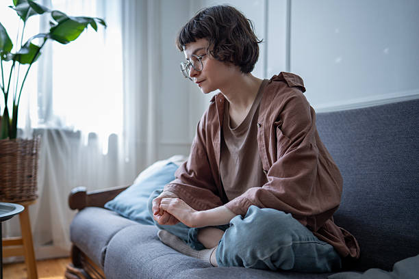 Nervous woman sitting cross legged on couch stressed fidgeting with hands feels insecure, overload.