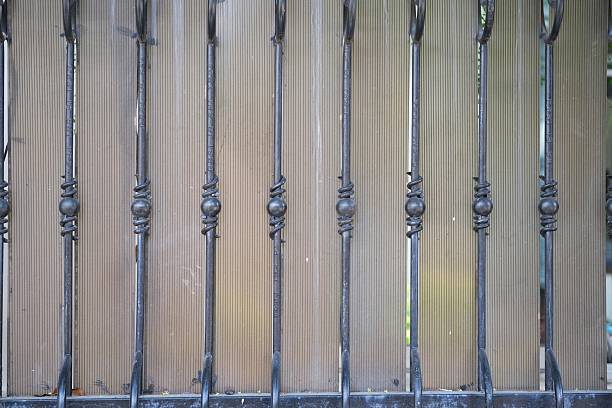 Detailed view of decorative black wrought iron fence featuring vertical bars and ornamental knots, installed in front of a wooden panel wall.