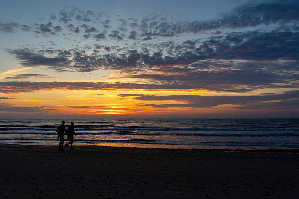 Active senior couple enjoying a day out at beach  in casual wear running along the coast at sunset.