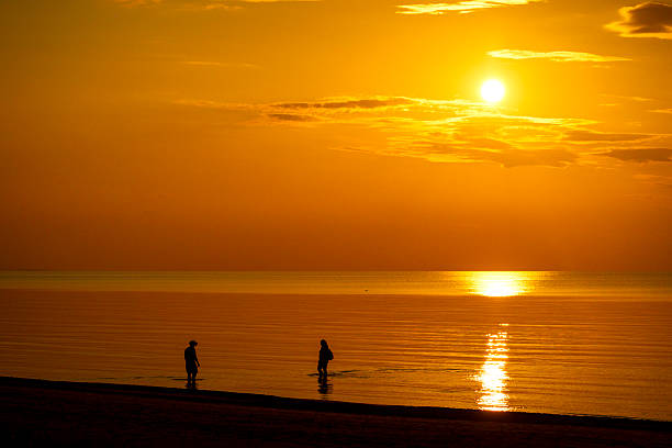 A beautiful summer sunset scenery with people silhouettes walking on a beach, enjoying Baltic Sea costline. Evening landscape of Latvia, Europe.