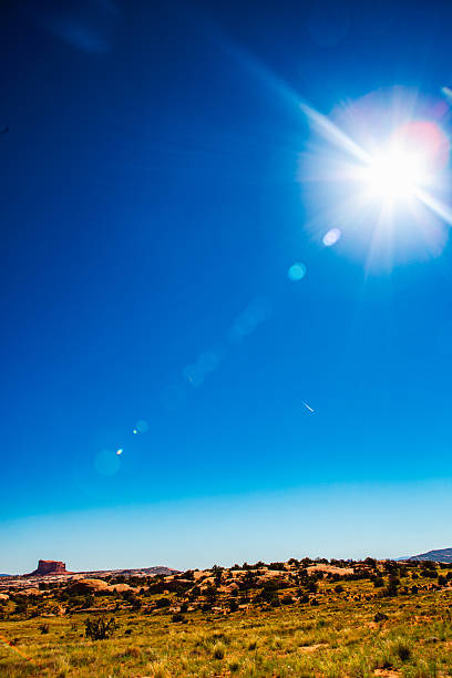 A vertical composition captures the desert plain beneath a deep blue sky, where the sun dominates the frame — its blinding radiance scattering through the lens in a cascade of orbs and flares.The faint mesa on the horizon anchors the composition, grounding the viewer as the rest of the frame dissolves into pure, celestial frequency.This is light as vibration — the visual sound of stillness.It transforms the infinite quiet of the previous frames into a hum of energy that fills the air without a voice.The small contrail, recurring like a rhythmic echo, ties this moment back to the human trace from The First Echo, now reduced to insignificance before the solar force.