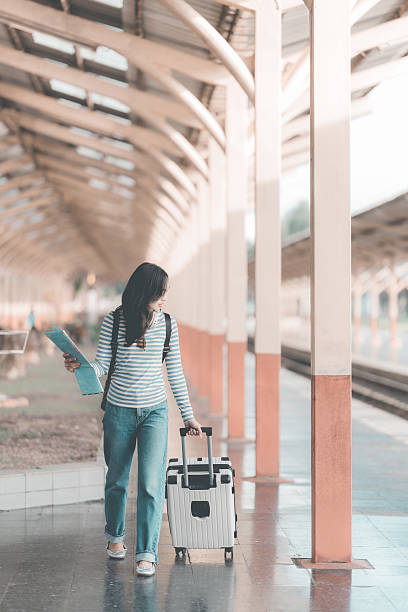 istock Asian woman with backpack looking forward while standing at train station, holding luggage, waiting for train to depart at busy station, excited about the journey. 2244475799