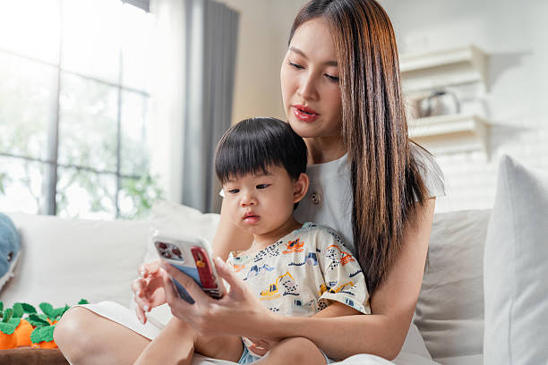 istock Smiling mother shares smartphone content with curious son while relaxing together on comfortable living room sofa, enjoying quality bonding time and digital entertainment at home 2244482618