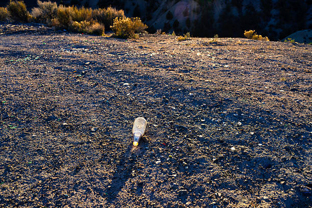 Trash left in area where people litter and break bottles, glittering in backlit golden hour light.
