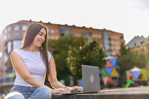 istock Beautiful student typing seminar for the exam and  using laptop while sitting on the bench in the public park. 2244491886