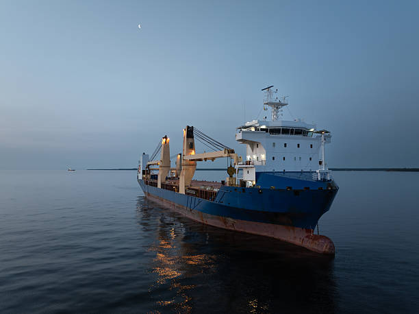 istock A large general cargo ship with illuminated cranes is anchored in calm sea at dusk, under a crescent moon. 2244515323