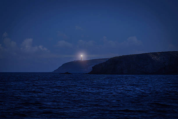 Lighthouse beam piercing the dark night sky over the Aegean Sea and coastline
