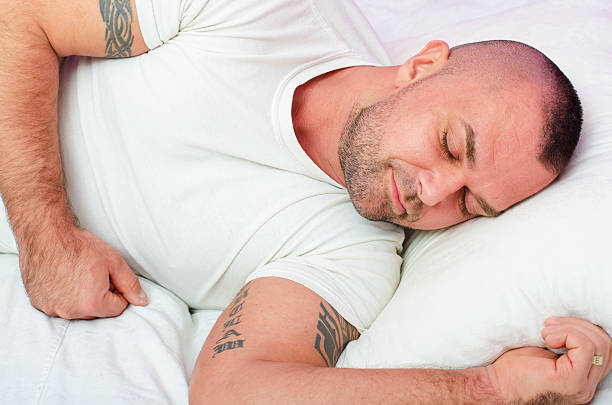 Domestic guy napping on couch at TV watching closeup. Portrait of tired dark-haired man falling asleep on pillow cozy home sofa at night. Handsome television viewer feeling sleepy uninterested movie.