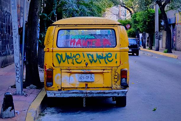 Mexico City, Mexico – October 29, 2025: A yellow van covered in graffiti parked along a shaded street in the Escandon neighborhood of Mexico City.