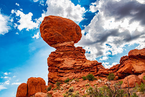 The towering formation of Balanced Rock dominates the sky, no longer framed by tension but by rhythm.The desert’s geometry softens here — lines blur into motion, and the light dances across the sandstone surface like skin touched by air.Above, the clouds fracture and swirl with hypnotic movement, revealing glimpses of deep blue sky between them.The contrast between solidity and motion — red stone against living atmosphere — creates the illusion that the landscape itself has a heartbeat.This frame captures the precise moment when stillness becomes rhythm, when the weight of eternity finds tempo.The balanced stone, emblem of permanence, now seems alive — not resisting gravity but swaying in harmony with the wind.