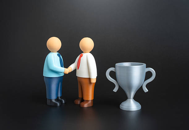 Two office workers shake hands near the winner's trophy. Recognition of success