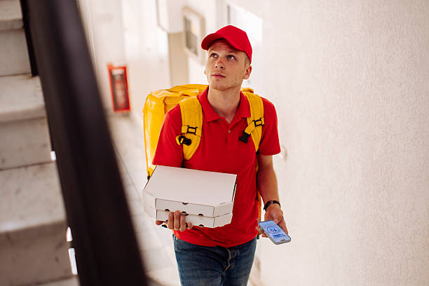 istock Delivery Worker in Red Uniform with Pizza Box and Yellow Backpack in Hallway 2244540915