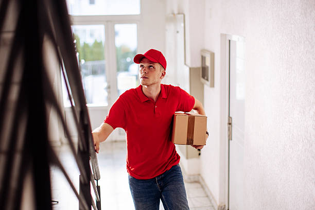 istock Delivery Man in Red Uniform Carrying Package Through Hallway Ready for Front Door 2244540941