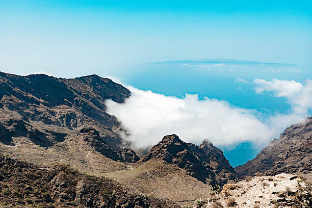 A beautiful atmospheric view from an observation deck of a volcanic mountain range shrouded in white clouds on a clear day with a blue sky on the island of Tenerife, medium-sized shot, side view. Concept: natural backgrounds, mountain landscapes.