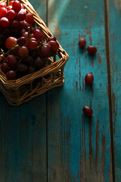 A basket filled with red grapes is positioned on a blue wooden table, showcasing fresh and juicy fruits.