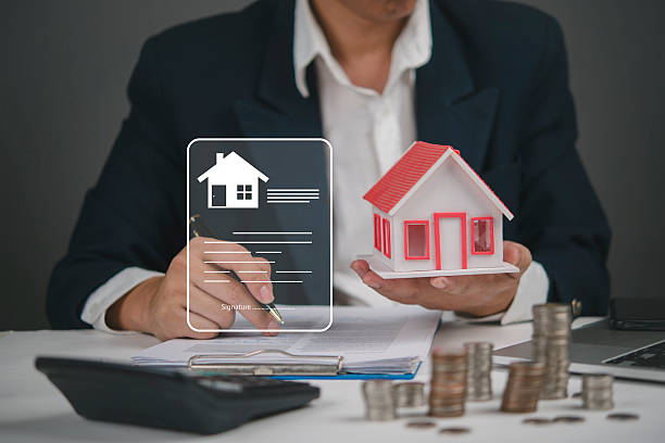 istock Real estate agent signing property contract while holding house model and calculating mortgage payment with stacked coins. Concept of home investment, housing loan, and financial planning. 2244558701