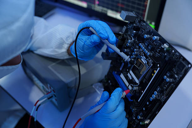 Engineers in sterile suits work at a semiconductor manufacturing plant using microscopes in a lab.