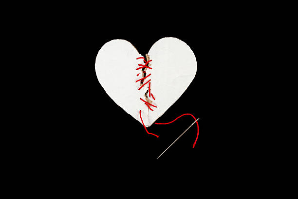 istock Broken white cardboard heart sewed together with a needle and red thread on black background, marriage counseling concept 2244568986